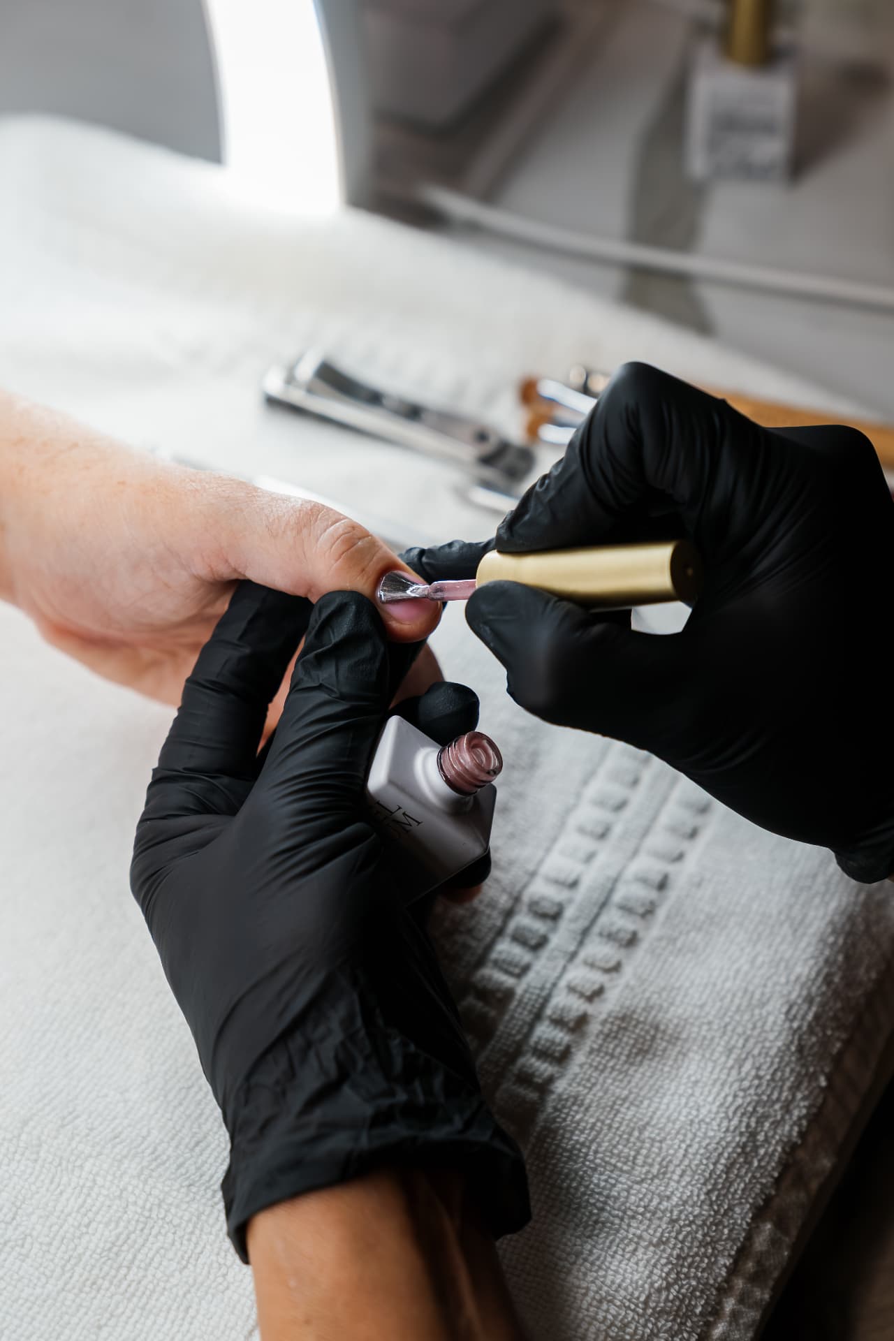 Nail technician working on a client's nails under a lamp