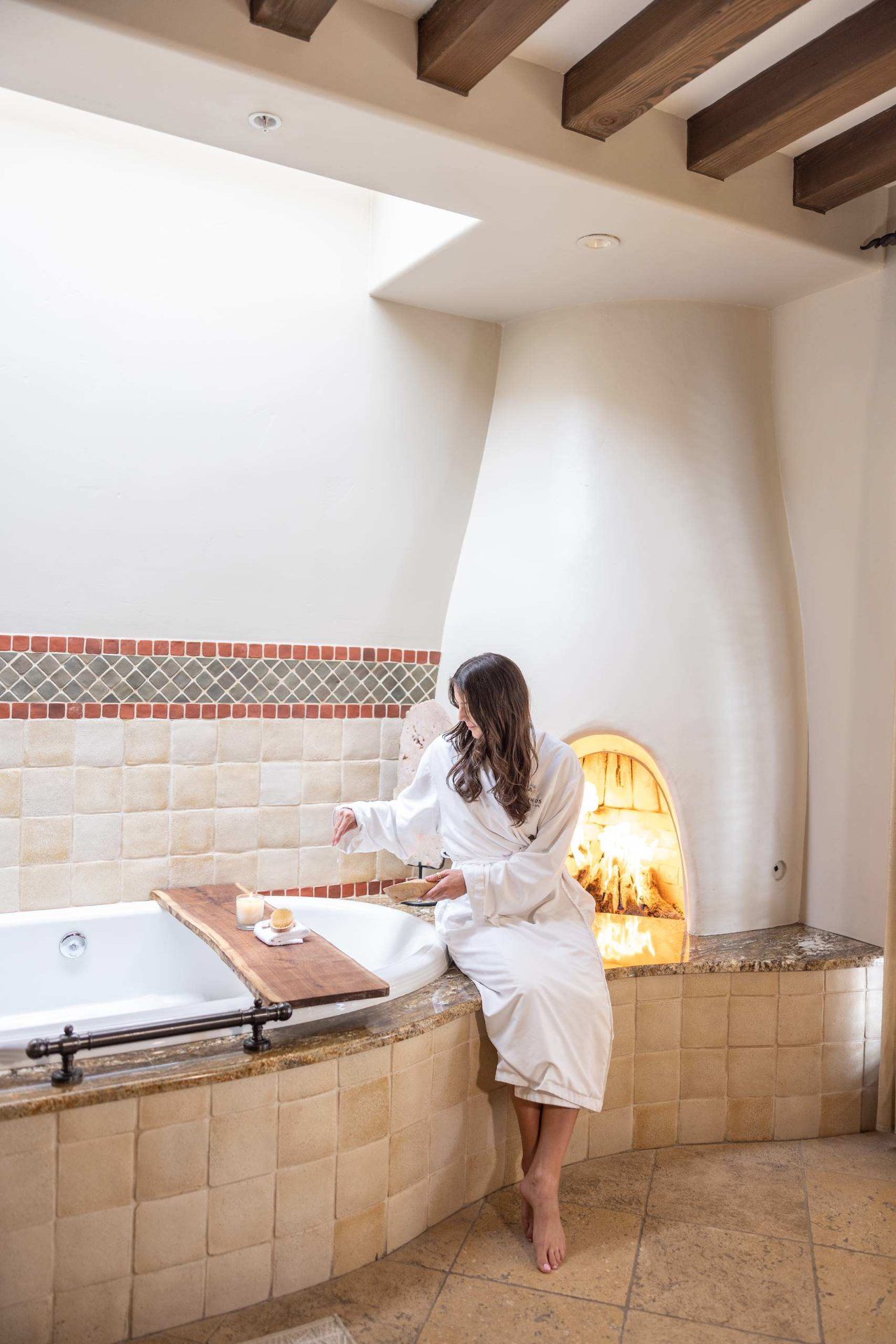 Guest in robe beside soaking tub and adobe fireplace