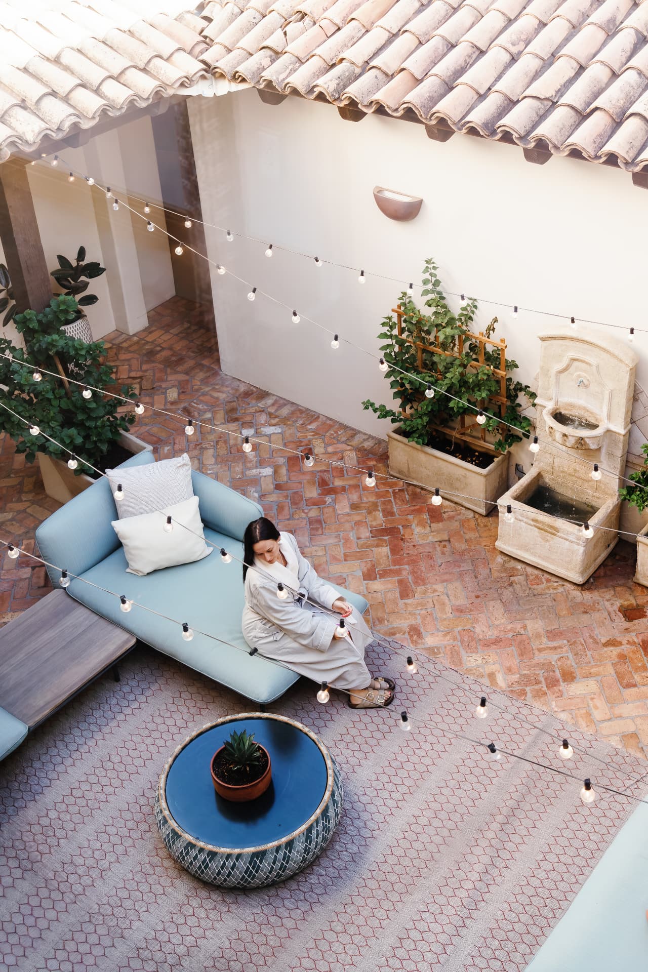 Guest in robe resting on a courtyard daybed beneath string lights